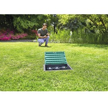 Tuinlandschap met een man die een smartphone bedient, op de voorgrond een in het gazon ingebouwde stroomverdeler met open deksel.