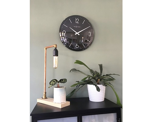 Zwarte wandklok naast tafellamp en kamerplanten op een kast
