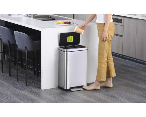 Roestvrijstalen afvalemmer met voetpedaal in een keuken, een persoon gooit een papieren beker weg