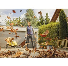 Man gebruikt een bladblazer om bladeren in een tuin te verwijderen.