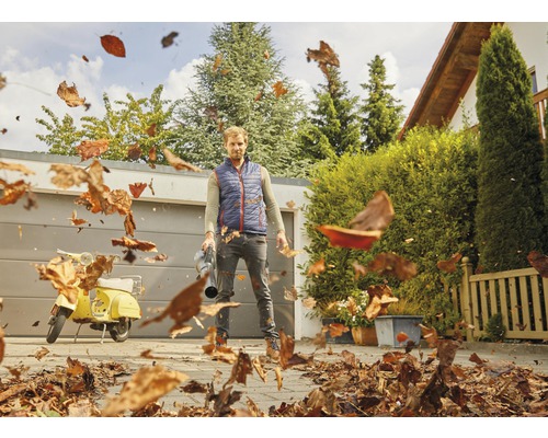 Man gebruikt een bladblazer om bladeren in een tuin te verwijderen.