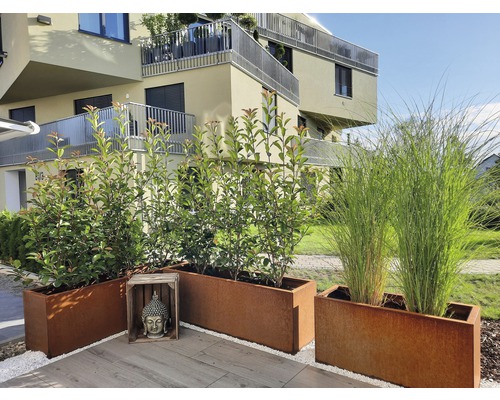 Decoratieve metalen plantenbakken op een terras voor een woongebouw.