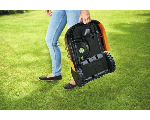 Een persoon draagt een robotmaaier over een gazon.