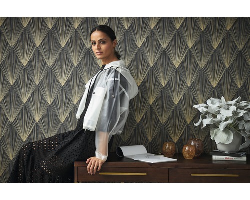 Scène met behang met patroon en een vrouw zittend op een bureau met een plant, vazen en boeken.