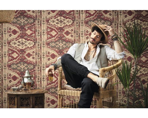 Man zit in een rotan stoel voor een muur met een rood patroon.