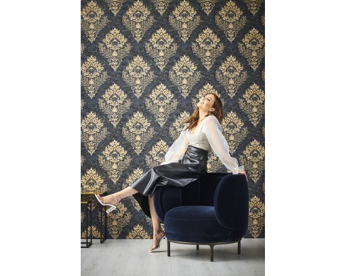 Vrouw zit op een fauteuil voor een muur met een patroonbehang