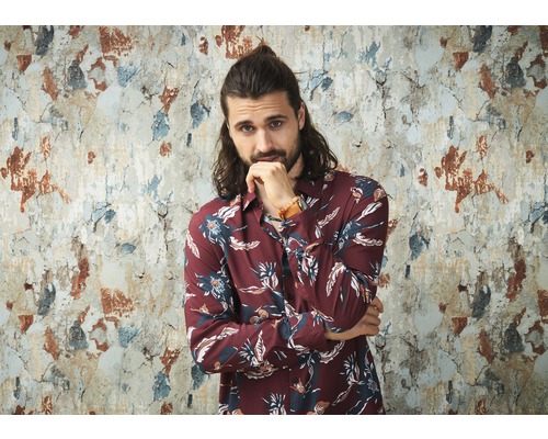 Man met bloemenhemd voor een beschadigde muur