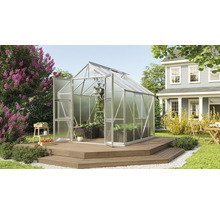 Kas met open deur op een houten terras in een tuin met bloemen en een woonhuis.