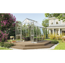 Glazen kas op houten terras in een tuin met planten en een huis op de achtergrond.