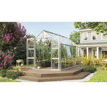 Kas in de tuin met planten en tuinmeubelen op een houten terras voor een woonhuis.