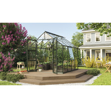 Tuinkas op een houten terras in een tuin met planten en een woonhuis op de achtergrond.