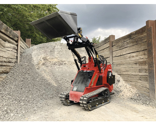 Rode minilader met schep voor een stapel grind