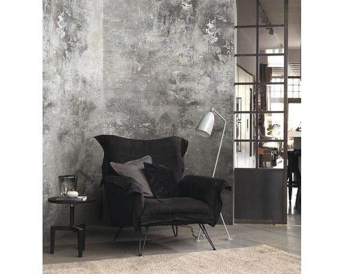 Woonkamer met zwarte fauteuil, vloerlamp en bijzettafel voor een wand met pleisterstructuur