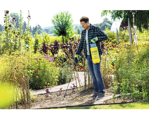 Een man gebruikt een Gloria tuinspuit in een bloeiende tuin.