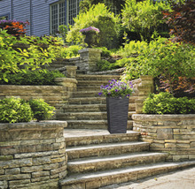 Hoge plantenbak met bloemen op een stenen trap in de tuin.