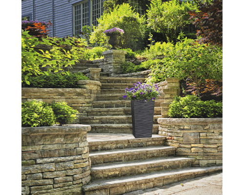 Hoge plantenbak met bloemen op een stenen trap in de tuin.