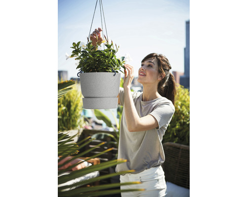 Vrouw bekijkt hangende bloempot met planten op een balkon.
