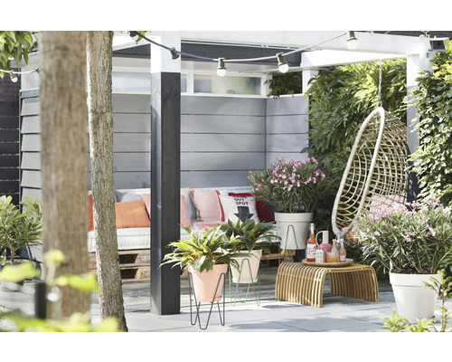 Gedecoreerde tuin met zitje, hangstoel, bijzettafel, planten en lichtslinger.