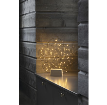 Decoratieve lichtgevende bol met LED-lampjes op een grijs meubelstuk voor een houten wand.