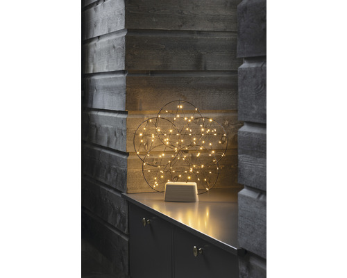 Decoratieve lichtgevende bol met LED-lampjes op een grijs meubelstuk voor een houten wand.