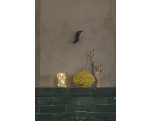 Decoratieve opstelling met kaars, vaas, houten hand en takken op een schoorsteenmantel.