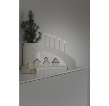 Decoratieve kerstscène met lichtboog, sterkaarsen, kleine huisjes en een potplant.