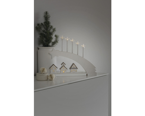 Decoratieve kerstscène met lichtboog, sterkaarsen, kleine huisjes en een potplant.