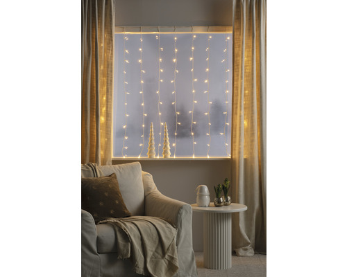 Gezellige woonkamer met lichtslingers, gordijnen, fauteuil en bijzettafel voor een warme sfeer.