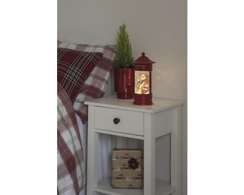 Nachtkastje met kerstdecoratie, inclusief een sneeuwbol met een kerstmanmotief en een potplant