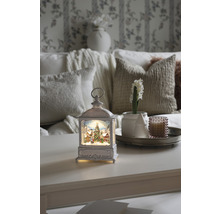 Decoratieve lantaarn met kerstmotief op een tafel, omringd door woonaccessoires voor een feestelijke sfeer