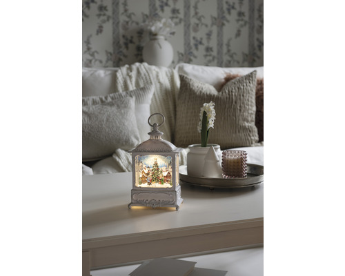 Decoratieve lantaarn met kerstmotief op een tafel, omringd door woonaccessoires voor een feestelijke sfeer