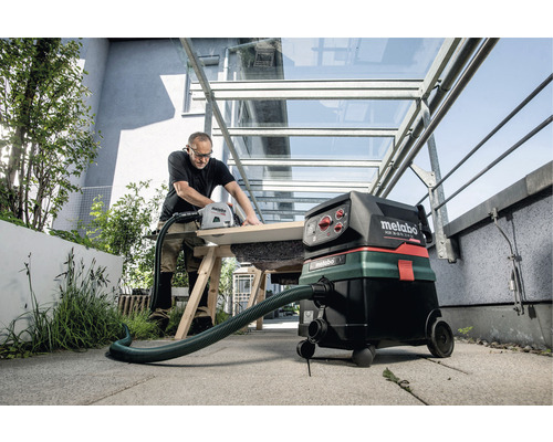 Vakman zaagt hout met handzaag en industriële stofzuiger