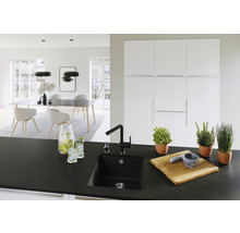 Lichte keuken met zwarte spoelbak, kraan, kruiden in pot, snijplank en eettafel