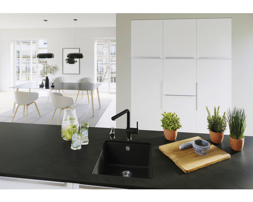 Lichte keuken met zwarte spoelbak, kraan, kruiden in pot, snijplank en eettafel