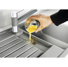 Spoelbak met kraan en hand die een glas vloeistof uitgiet