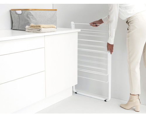 Opvouwbaar wasrek naast een kast met wasmand en handdoeken