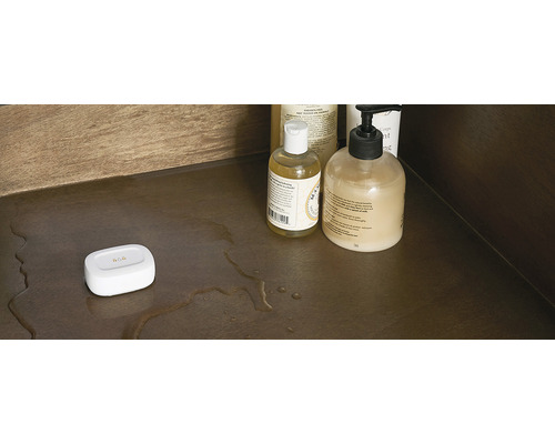 Scene met badkamerbenodigdheden en een witte vochtsensor op een plank met waterresten