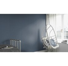 Lichte, moderne slaapkamerinrichting met schommelstoel, bed en blauw geschilderde muur
