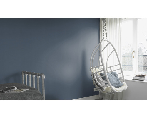 Lichte, moderne slaapkamerinrichting met schommelstoel, bed en blauw geschilderde muur