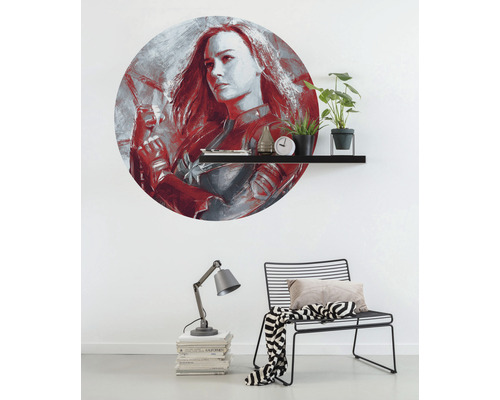 Wanddecoratie met Captain Marvel motief boven een plank met decoraties, lamp en stoel in de kamer.