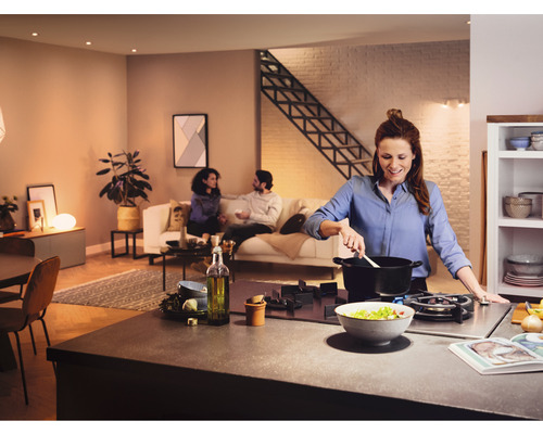 Open keuken met een vrouw die kookt, terwijl twee mensen in de woonkamer praten.