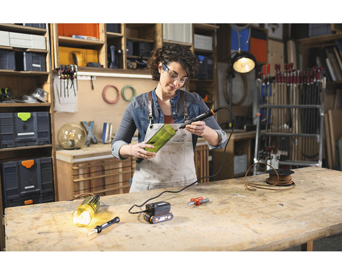 Vrouw werkt met een multifunctioneel gereedschap aan een glazen fles in een werkplaats.
