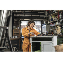 Vrouw verwijdert verf met een heteluchtpistool van een houten kast in een werkplaats.