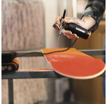 Een persoon gebruikt een Worx airbrushpistool om een houten plank te schilderen.