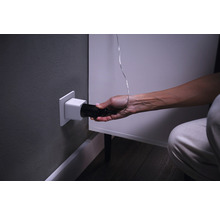 Een persoon steekt een zwarte stekker in een wit stopcontact in de muur.