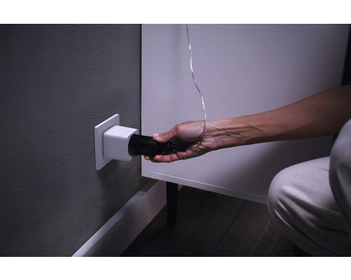 Een persoon steekt een zwarte stekker in een wit stopcontact in de muur.