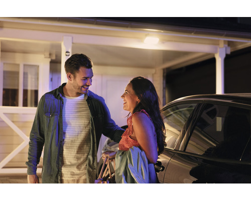 Een lachend paar voor een huis en auto.