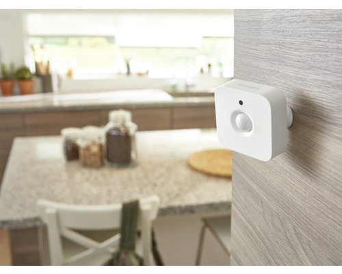 Witte Philips Hue bewegingsmelder gemonteerd op een licht houten oppervlak in een lichte, georganiseerde keuken.