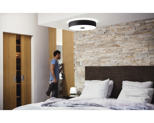 Slaapkamer met bed, stenen muur, plafondlamp en man die een schuifdeurkast opent