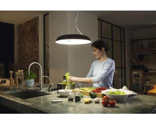 Vrouw bereidt salade onder een moderne hanglamp in een lichte keuken